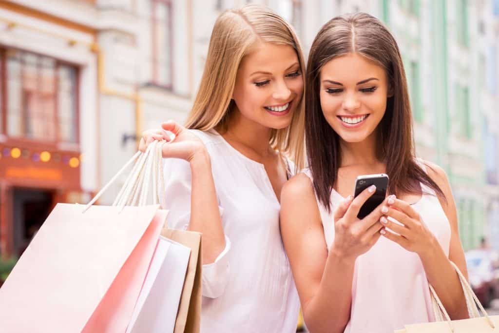 Two women holding shopping bags looking at a smartphone